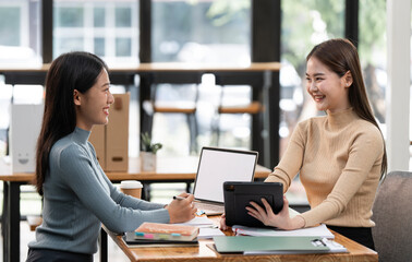 Two business women sit at desk discuss project details, diverse female colleagues met in office,