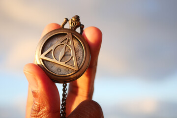 A Hand Holding an Intricate and Detailed Pocket Watch Beneath a Beautiful Scenic Sky