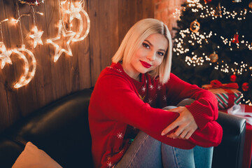 Photo of nice young blonde girl hugging knees cozy wear christmas sweater enjoy cozy x-mas party...