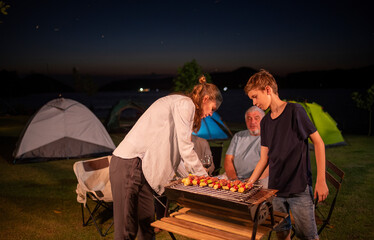 Family barbecue during a camping trip is grilling food on a portable barbecue grill, with holding glasses of red wine as they enjoy the moment together shared moments family holiday camping trip.