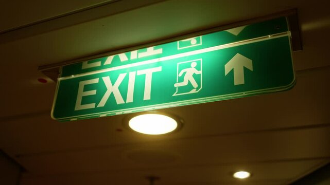 Bright illuminated exit sign indoors with green background and directional arrow, symbolizing emergency exit wayfinding in a safety-focused environment.