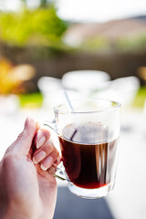 hand holding coffee in clear mug in front of blurred home interior background, habits and lifestyle concept