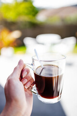 hand holding coffee in clear mug in front of blurred home interior background, habits and lifestyle concept