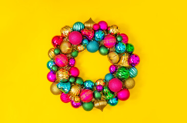 Beautiful Christmas wreath made of colorful shiny baubles on yellow background, top view