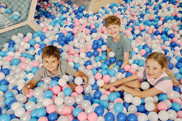 Happy little friends looking at camera with smiles while sitting among multi color balloons on playground