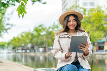 Asian female tourist using tablet for travel booking near Tha Phae Gate in Chiang Mai. Young woman planning itinerary or hotel arrangements while exploring city on vacation.