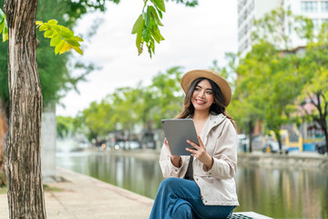 Asian female tourist using tablet for travel booking near Tha Phae Gate in Chiang Mai. Young woman...