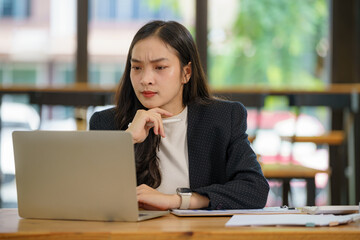 Beautiful Asian businesswoman using a laptop working in an office and depressed.