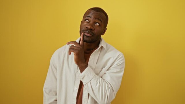 African american man wearing shirt standing thinking with chin on finger looking up in doubt and wonder, concentrated over isolated yellow background