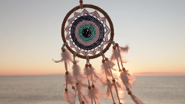 Dreamcatcher golden disk sun slow motion close up on background of blue sea sky in rays of sun at dawn in summer. Silhouette Indian talisman symbol. Boho style. Freedom, relax. Travel concept