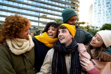 Happy multiracial friends laughing and having fun together during winter time outdoors in the city.