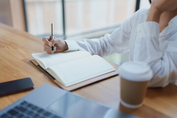 Business professional engaged in thoughtful writing and note-taking in a bright, modern workspace with a laptop and coffee cup on the table