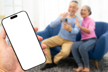 Empty white screen mockup smartphone with Happy smiling asian senior couple sitting on sofa and using smartphone while online video call.