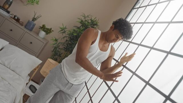 Young man leaning against window in bedroom looking dizzy indoors in a home setting surrounded by potted plants