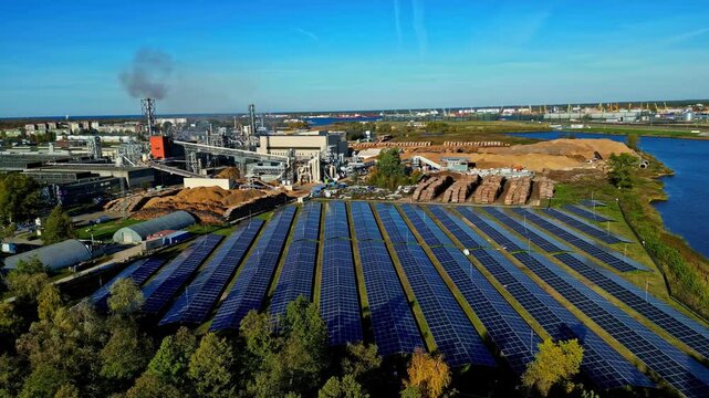 Aerial view of a large solar panel field close to a industrial plant, sunny day
