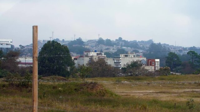 Street view through barbed wire fence showcasing Zone 18 favelas Guatemala City, endless stacked houses, cultural architecture - slow-mo