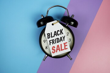 Black Friday Sale Word on price tag with alarm clock top view on purple geometric background