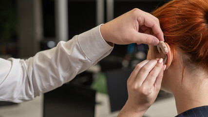 Man putting hearing aid on Caucasian red-haired woman. 