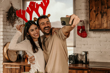 A happy morning couple with coffee, taking a selfie and  cuddling in the kitchen at their cozy apartment