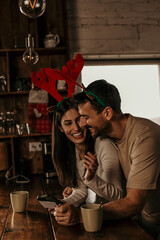 The couple enjoys online Christmas shopping together, standing at the kitchen table in their cozy home