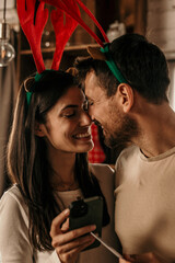A festive couple is shopping online on a phone on Christmas and New Year while hugging in morning at cozy home