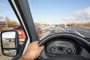 Driver's hand on the steering wheel of a car. View from the driver's cabin while driving on a highway.