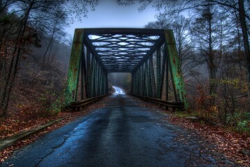 A weathered metal bridge spanning a misty road surrounded by autumn foliage.