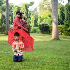 Indian couple posing for maternity baby shoot with their 5 year old kid. The couple is posing in a lawn with green grass and the woman is flaunting her baby bump in Lodhi Garden in New Delhi, India