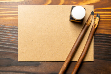 Two calligraphy reeds covered ink with inkwell and empty brown card on the table