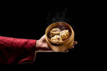 Chinese person holding dim sum dumpling on bamboo wooden basket bowl