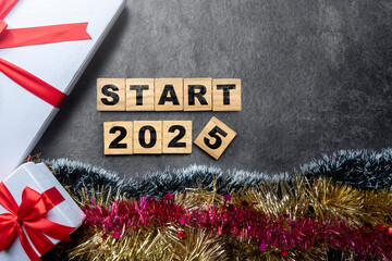 Wooden blocks with text of start 2025 and gift box with christmas ornament on black background