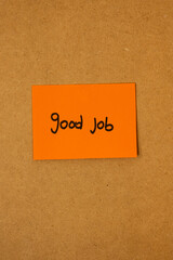 Vertical image of orange sticky note paper with text saying good job written on it, stuck on a brown board, concept of job recognition