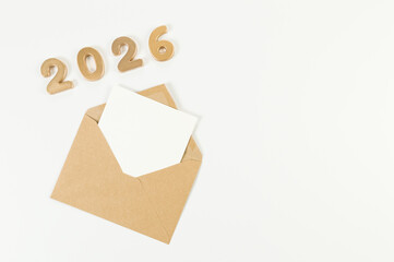 2026 Happy New Year. Top view of gold numbers, brown kraft envelope, white card on white background. Copy space, flat lay.