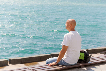 Man sits on a bench by the water, looking out at the ocean