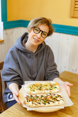 Happy beautiful young woman in eyeglasses and casual clothes eating pizza at a restaurant

