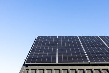 Fototapeta premium Modern house with solar panels stand-alone photovoltaic plant system on household metal sheet roof. Clear blue sky background. Clean alternative energy power concept, sustainable resources