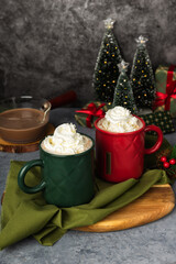 Red and green hot chocolate mugs and small Christmas tree. Sweet drink with cocoa and milk. A cozy homemade Christmas Eve evening