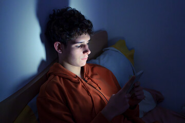 Teenager using a smartphone lying in bed late at night, playing games, watching videos online, and...