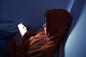 Teenager using a smartphone lying in bed late at night, playing games, watching videos online, and...