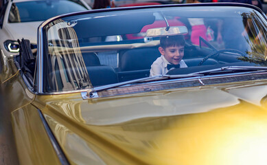 Happy kid in bow tie and shirt in front seat of vintage convertible car.
