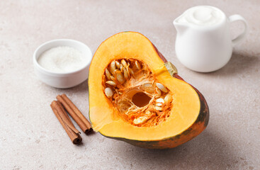 Cut raw orange pumpkin with seeds, cinnamon and sugar on a beige textured stone background. Preparing pumpkin for baking