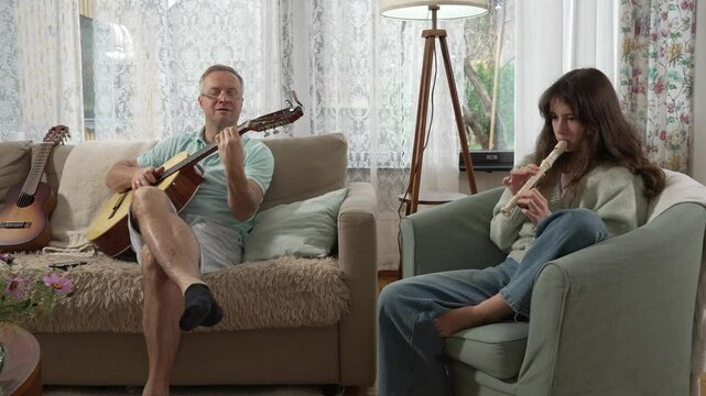 A middle-aged man and a 12-year-old girl enjoying a musical moment together, with him playing guitar and her playing a recorder flute in a cozy setting