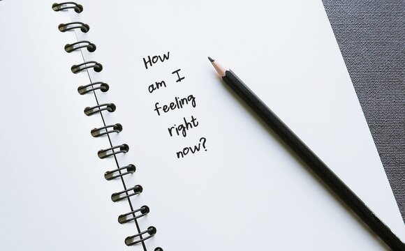Notebook with question HOW AM I FEELING RIGHT NOW? concept of checking in with yourself - key step toward understanding your mental and emotional state to attune to your own needs and feelings