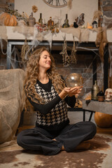 A woman gazes into a crystal ball in a cozy, autumn-themed setting decorated for Halloween