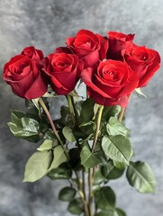 Naklejka premium Bouquet of seven red roses with green leaves against a gray background.