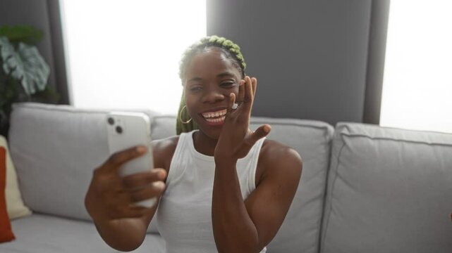 Woman showing engagement ring during video call in a cozy living room, capturing joy and excitement in a homely setting featuring a white sofa.