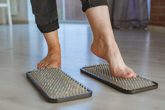 Human feet standing on Sadhu board at home, wooden board with a lot of hammered metal nails. Yoga Tool.