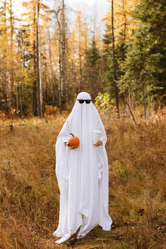Person standing in bedsheet ghost costume with pumpkin and coffeen and