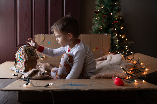 Young boy sitting in cardboard box playing with gingerbread house