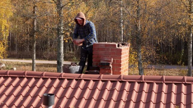 Brick chimney on red house rooftop being fixed by handyman, telephoto aerial